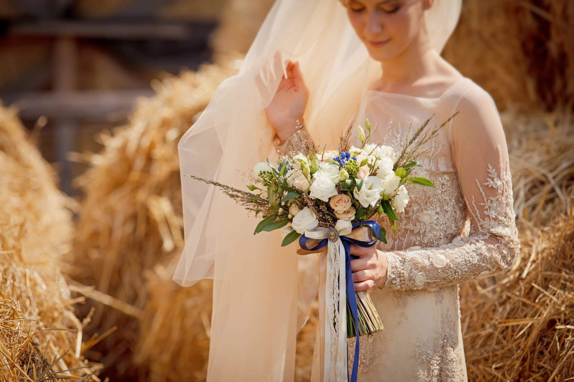 Braut mit Blumenstrauss vor Strohballen bei Hochzeit auf Bauernhof in NRW