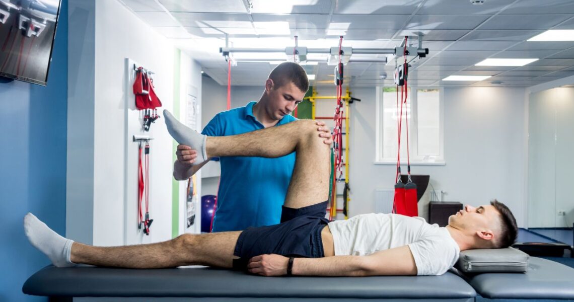 Sportmediziner Köln führt manuelle Mobilisation des Knies bei Patient auf Behandlungsliege durch