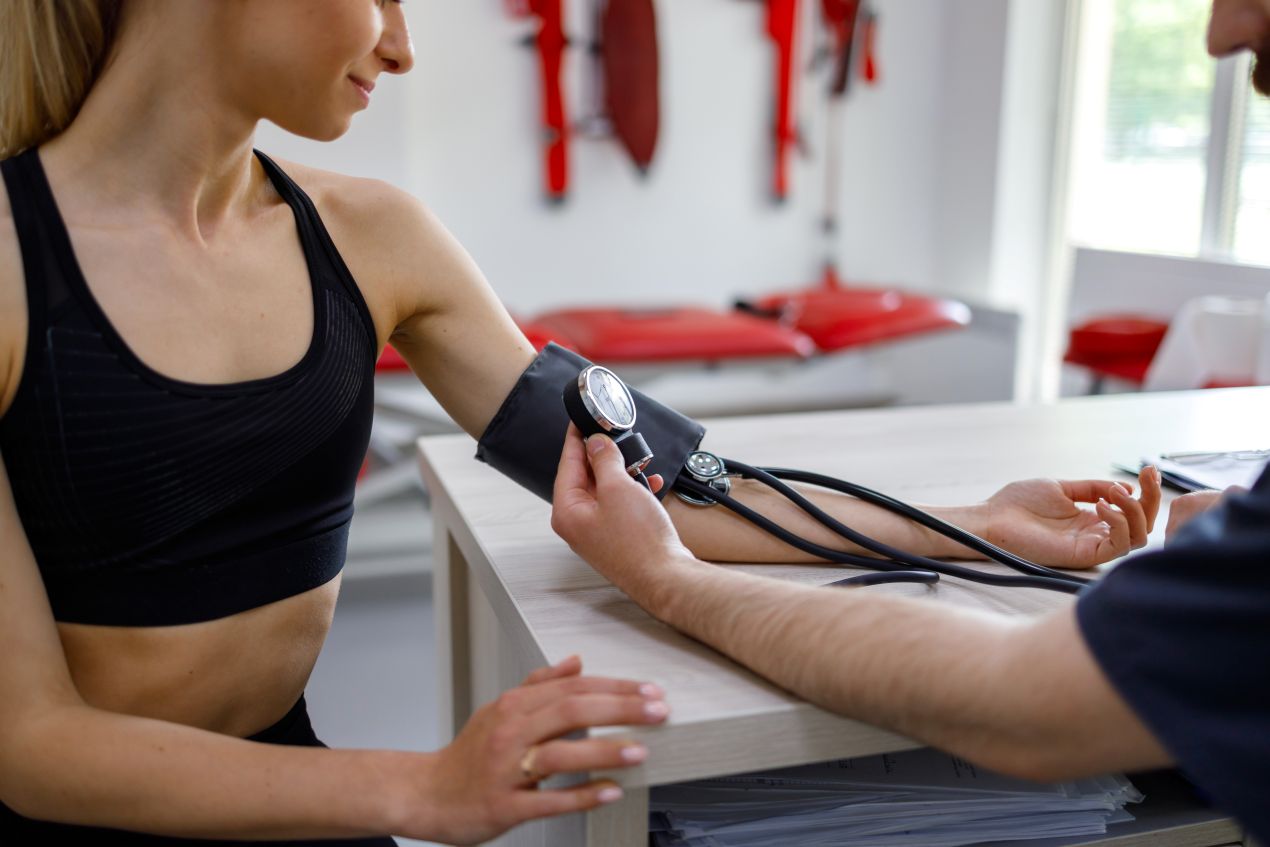 Sportmediziner Köln führt Blutdruckmessung bei sportlich aktiver Frau vor Trainingsberatung durch